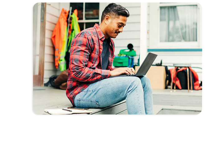 Photograph of a person sitting outside a house using a laptop computer