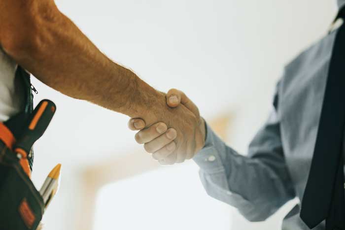 Photograph of a handshake between two people. One is wearing a toll belt on their waste and the other is wearing a button down shirt and tie