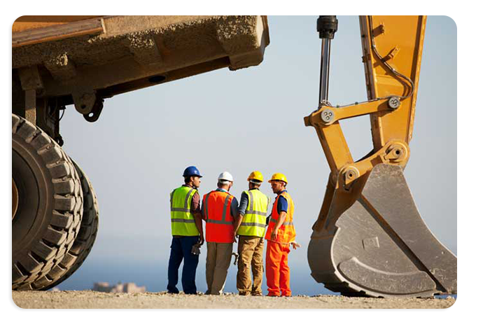 A photograph showing large earth moving machinery towering over four workers in safety vests and hard hats