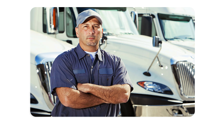 A photograph of a truck driver standing with folded arms. Behind them multiple large trucks can be seen.