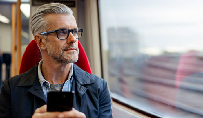 Photograph of a person seated on a moving train. The person is holding a mobile phone and looking out the train window