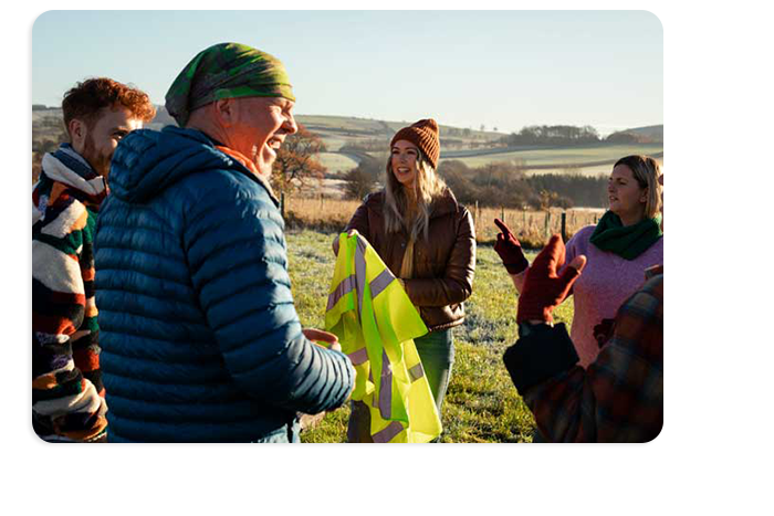 A group of people meet in a rural setting. One person is holding a high visibility safety vest