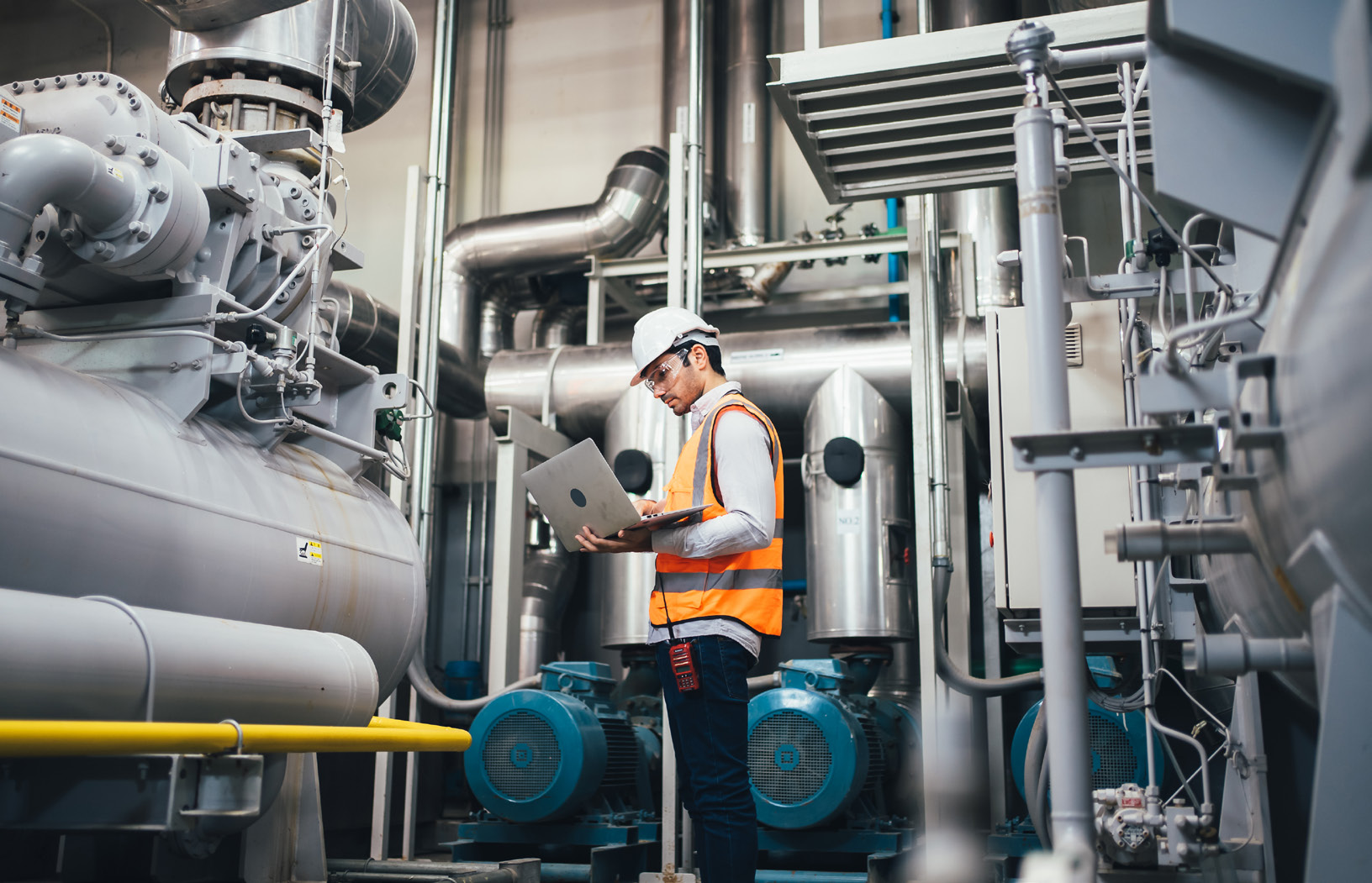 Engineer using a laptop to review data in an industrial plant room